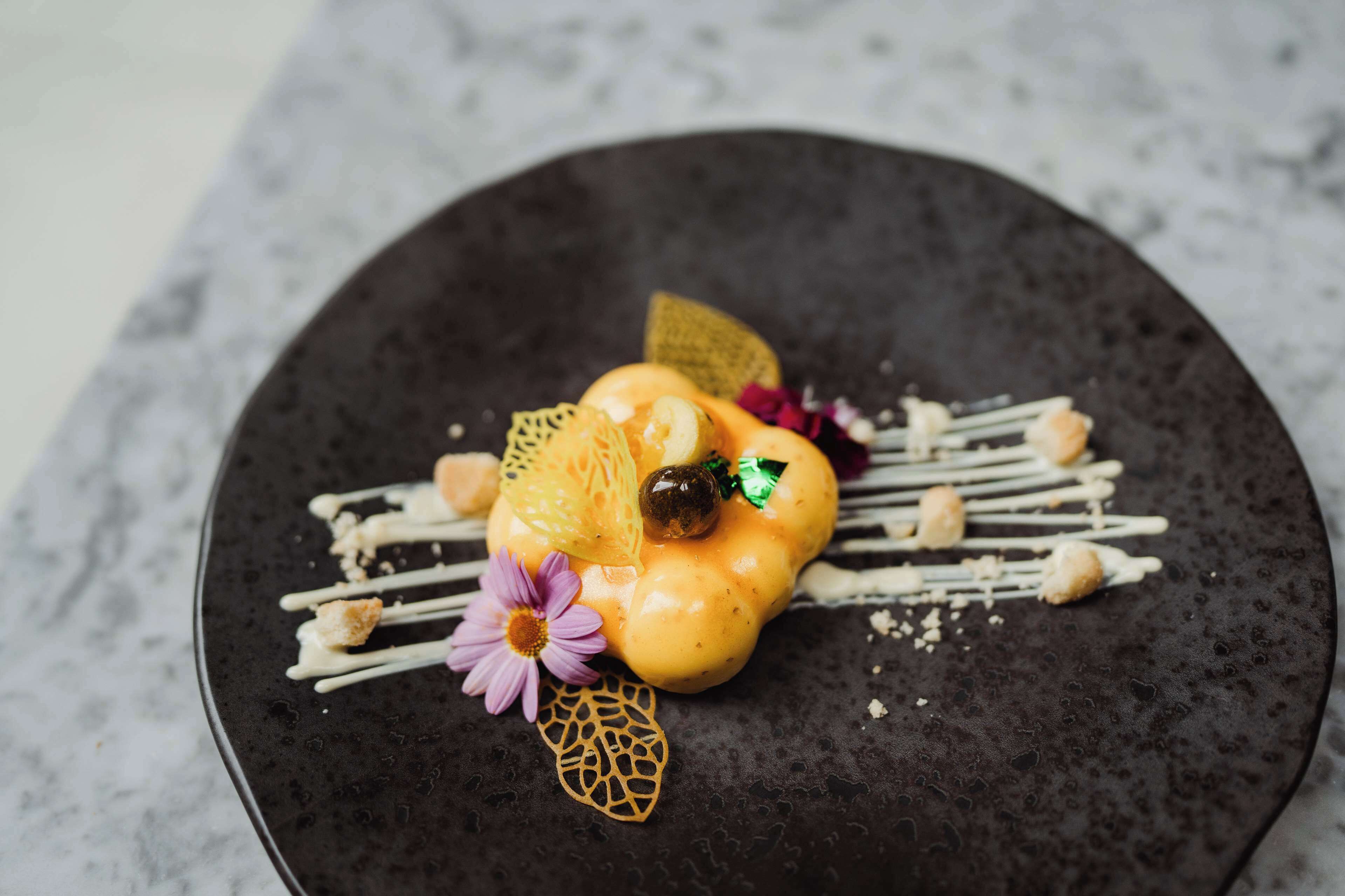 En dessert på en mørk tallerken med dekorative detaljer.
