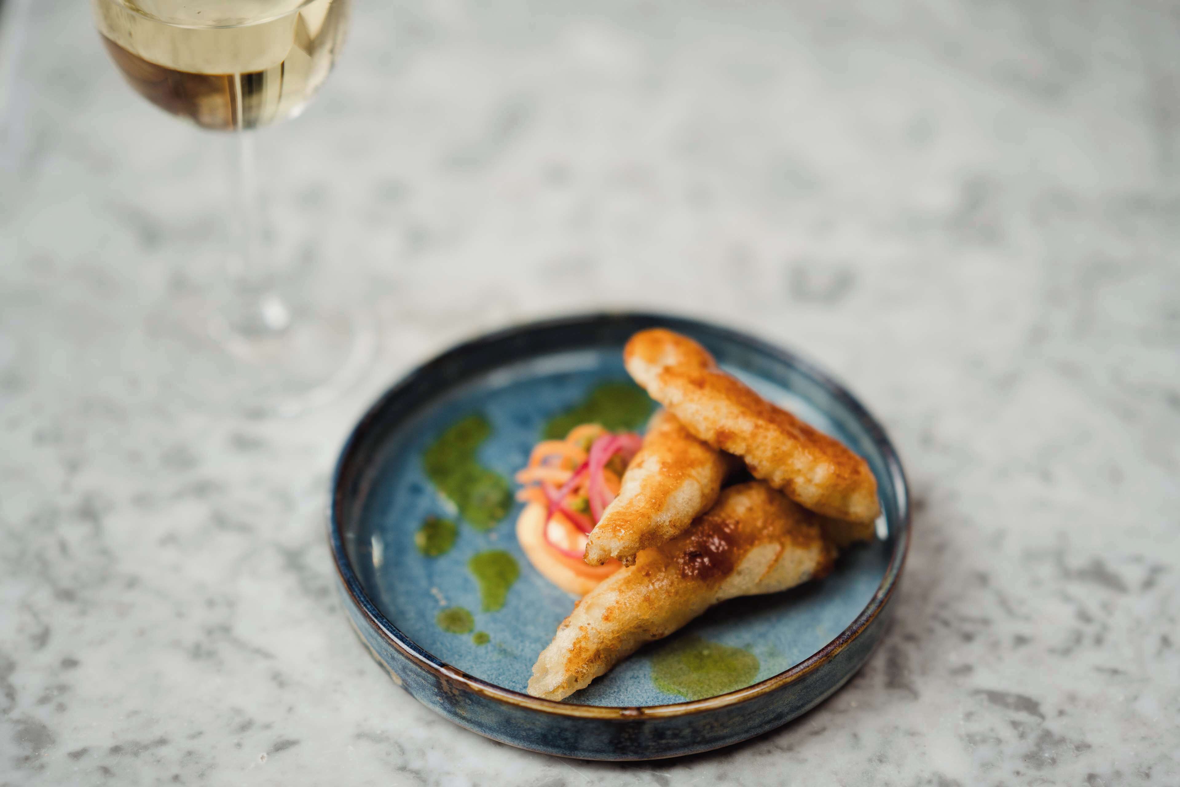 A plate with three fried items and a glass of white wine on a marble surface.