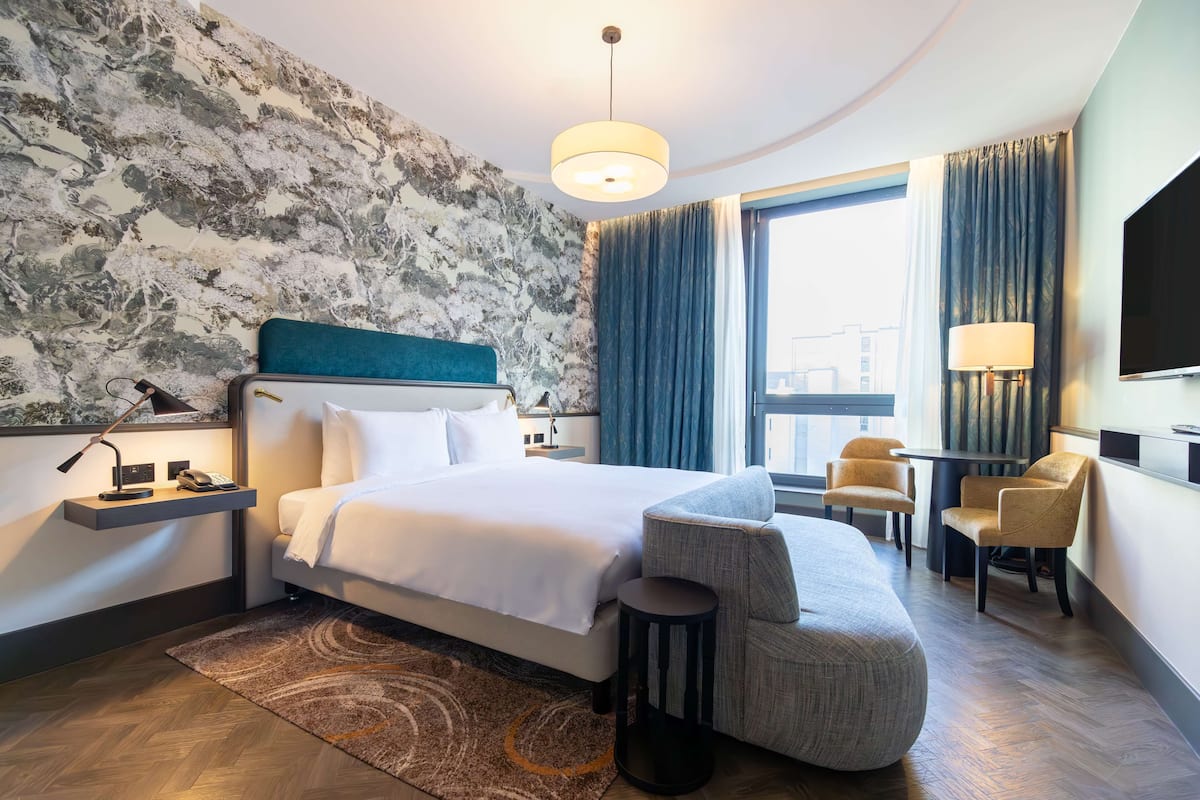 A modern hotel room with a large bed, a desk, and a seating area.