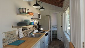 Una cocina compacta con encimera de madera, un lavamanos, una estufa y un microondas. Hay una puerta que da a otra habitación.