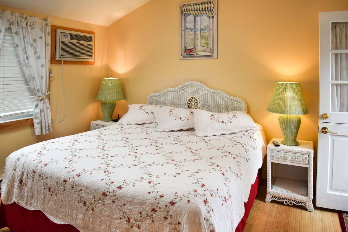A bedroom with a bed, two nightstands, a window with curtains, and a door.