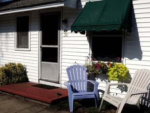 A white house with a green awning, two white Adirondack chairs, and a planter with flowers. - Shorelands Guest Resort and Cottages (Kennebunk)