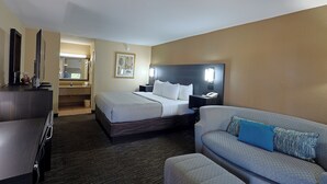 Une chambre d’hôtel équipée d’un lit, d’un canapé, d’un bureau, d’un miroir, d’une table de chevet et d’un téléviseur fixé au mur.
