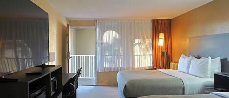 Habitación de hotel con dos camas, un escritorio con ordenador, una silla y un ventanal grande con cortinas.