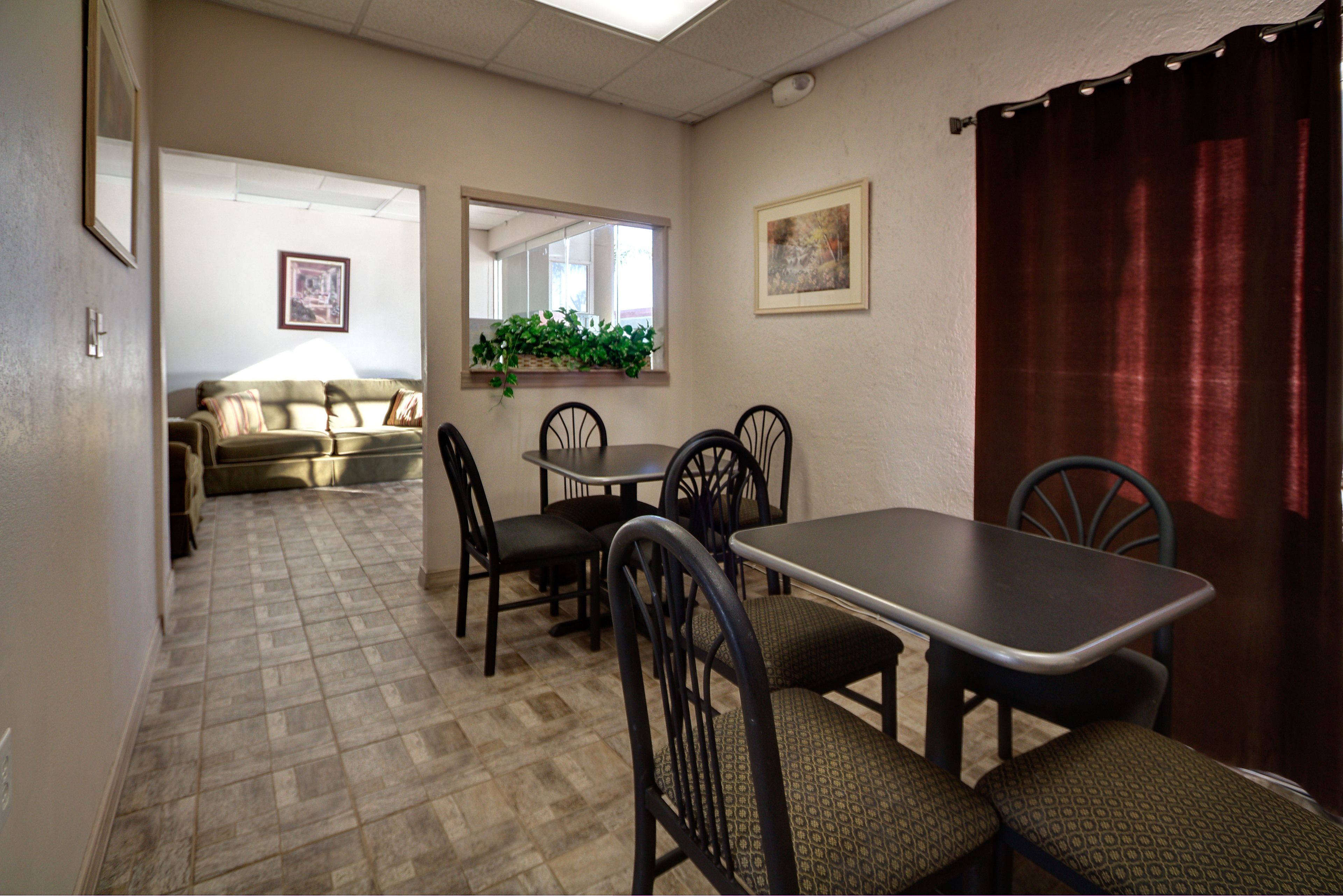 Un coin repas avec une table et des chaises, un canapé, une fenêtre avec une plante et un rideau rouge.