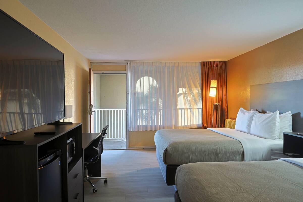 A hotel room with a bed, a desk with a computer, a chair, and a view of the outside.