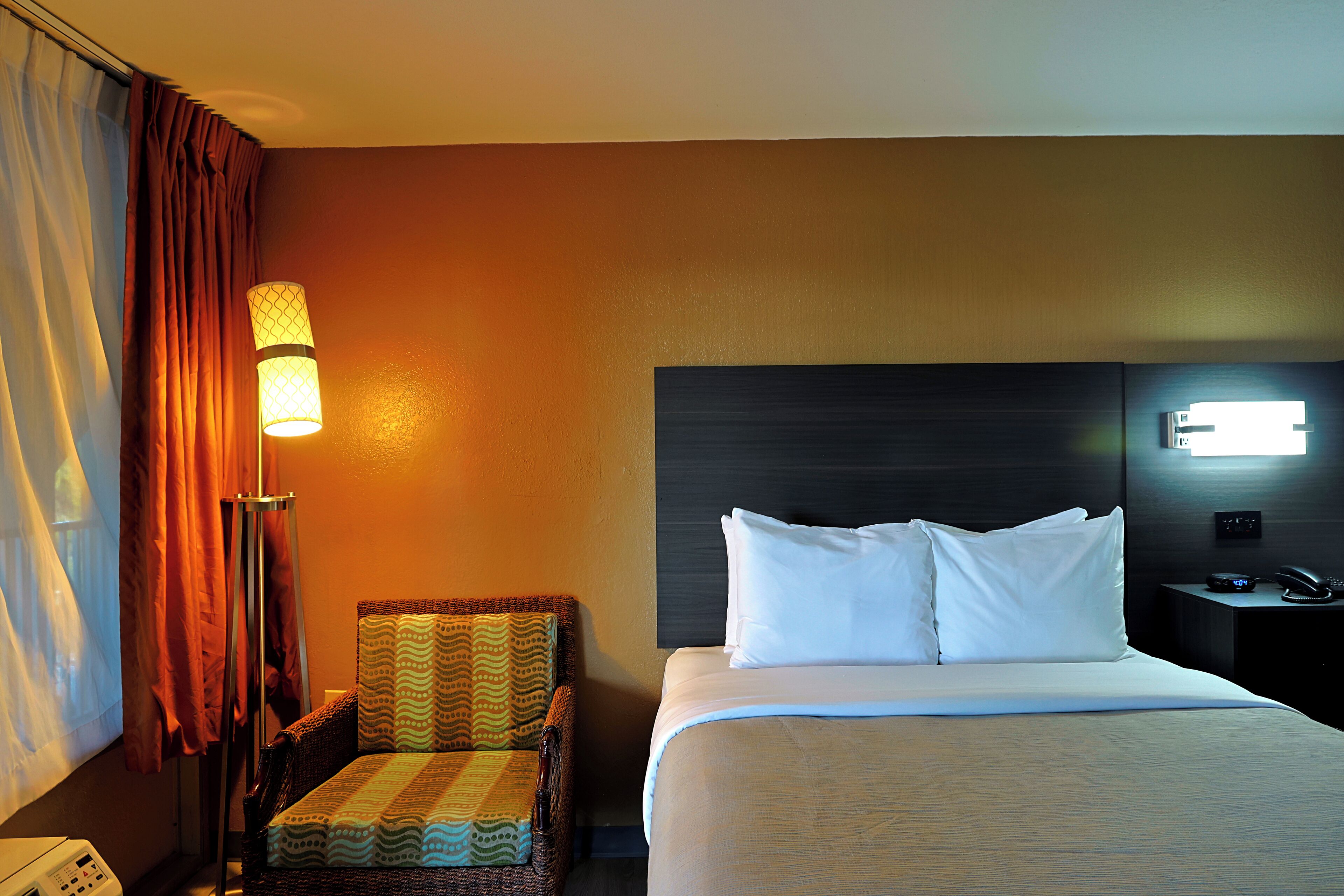 Una habitación de hotel con una cama, una silla, una lámpara y una mesita de noche con un teléfono.