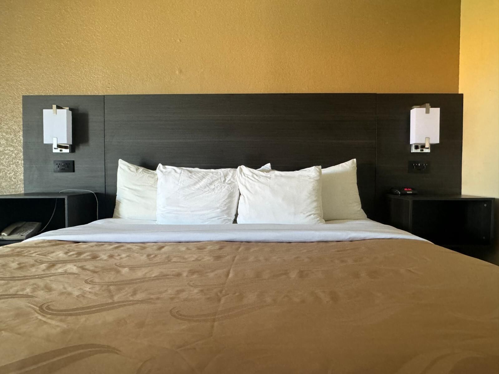 Hotellihuone, jossa on suuri sänky, kaksi yöpöytää, sängynpääty ja seinään kiinnitetyt lamput.
