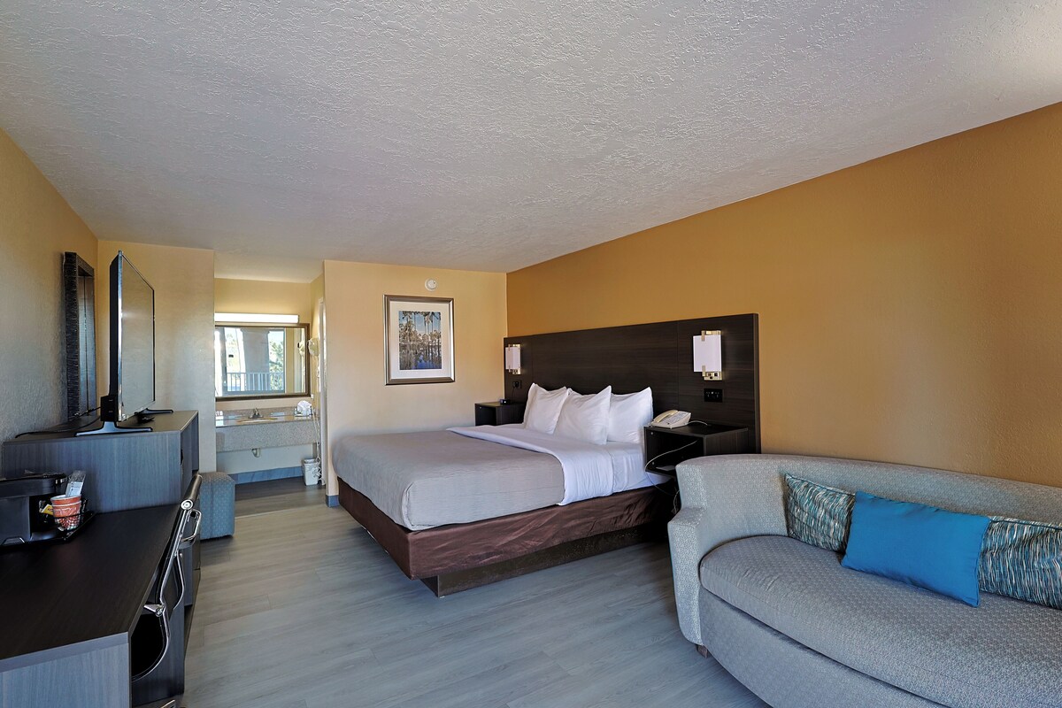 Quarto de hotel com cama, escrivaninha, sofá, banheiro e janela.