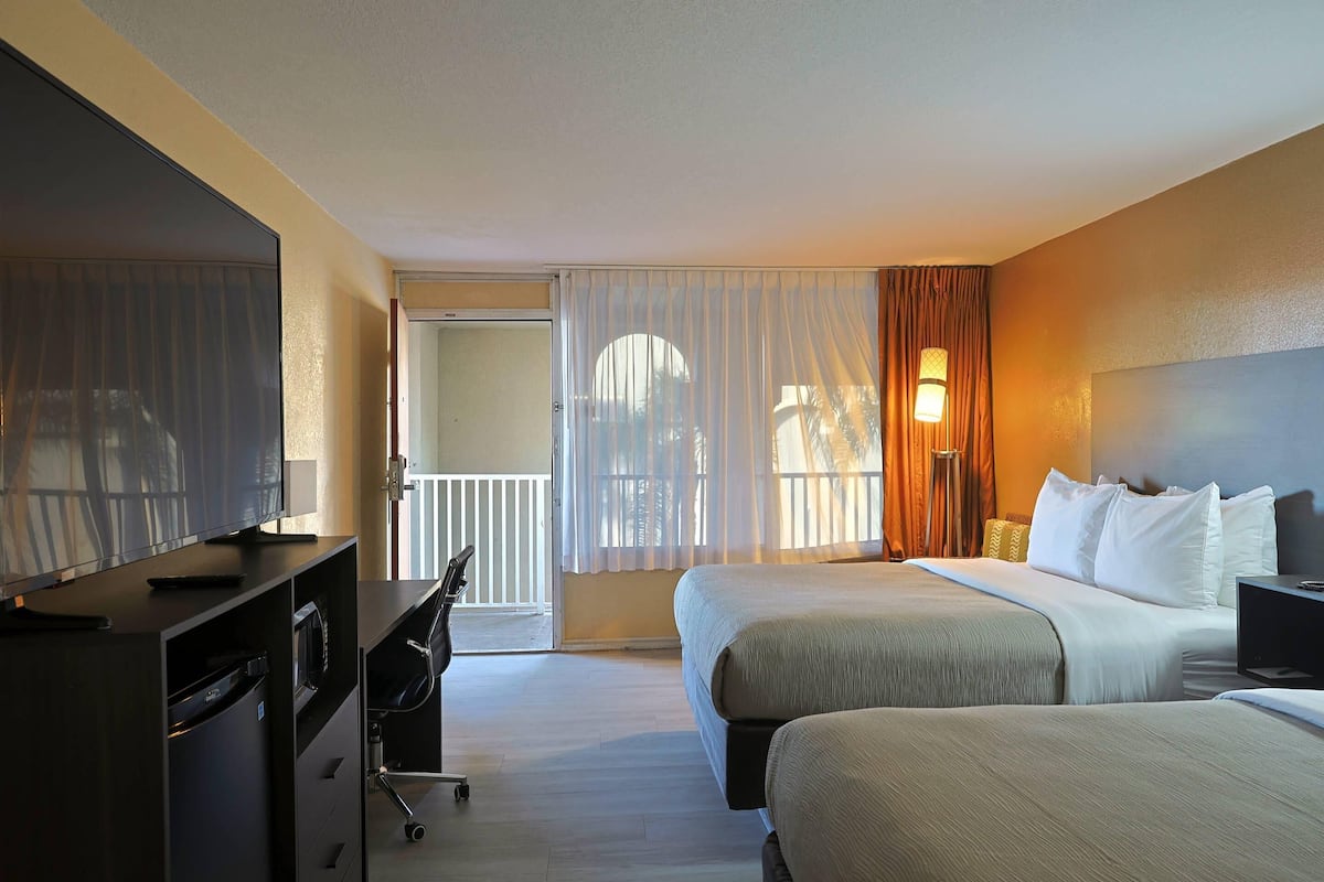 A hotel room with a bed, a desk with a computer, a chair, and a view of the outside.