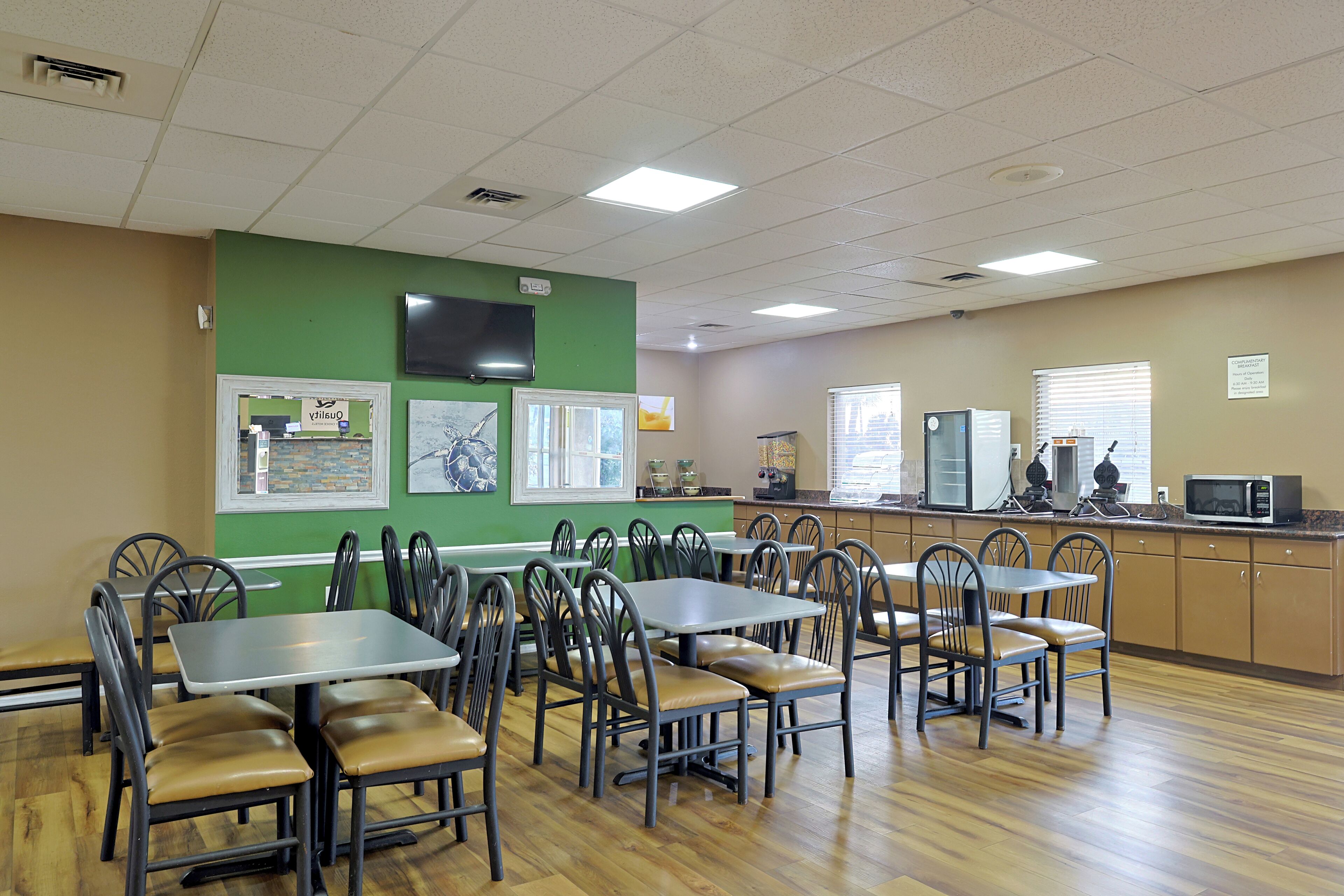 A dining area with multiple tables and chairs, a kitchen area with appliances, and artwork on the walls.
