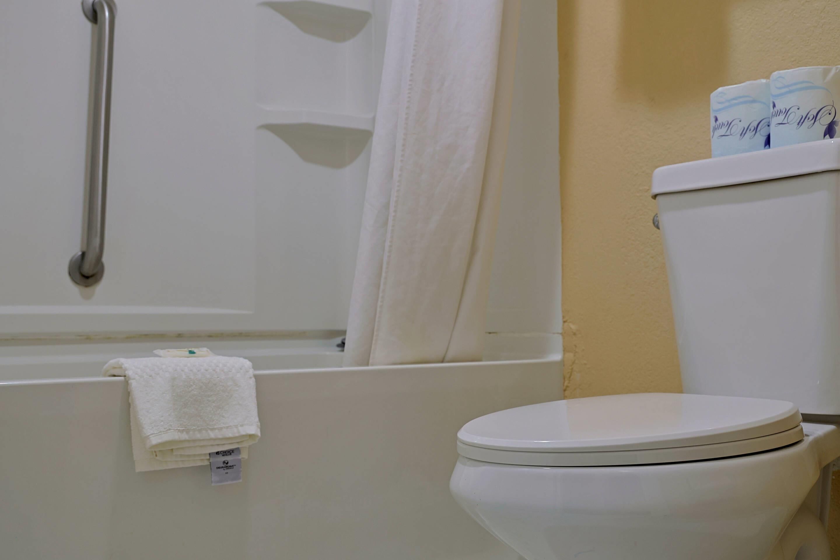 A bathroom with a white toilet, a white bathtub with a shower curtain, and a white towel on the floor.
