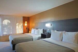 Habitación de hotel con dos camas, una mesita de noche, una lámpara y una ventana con cortinas.