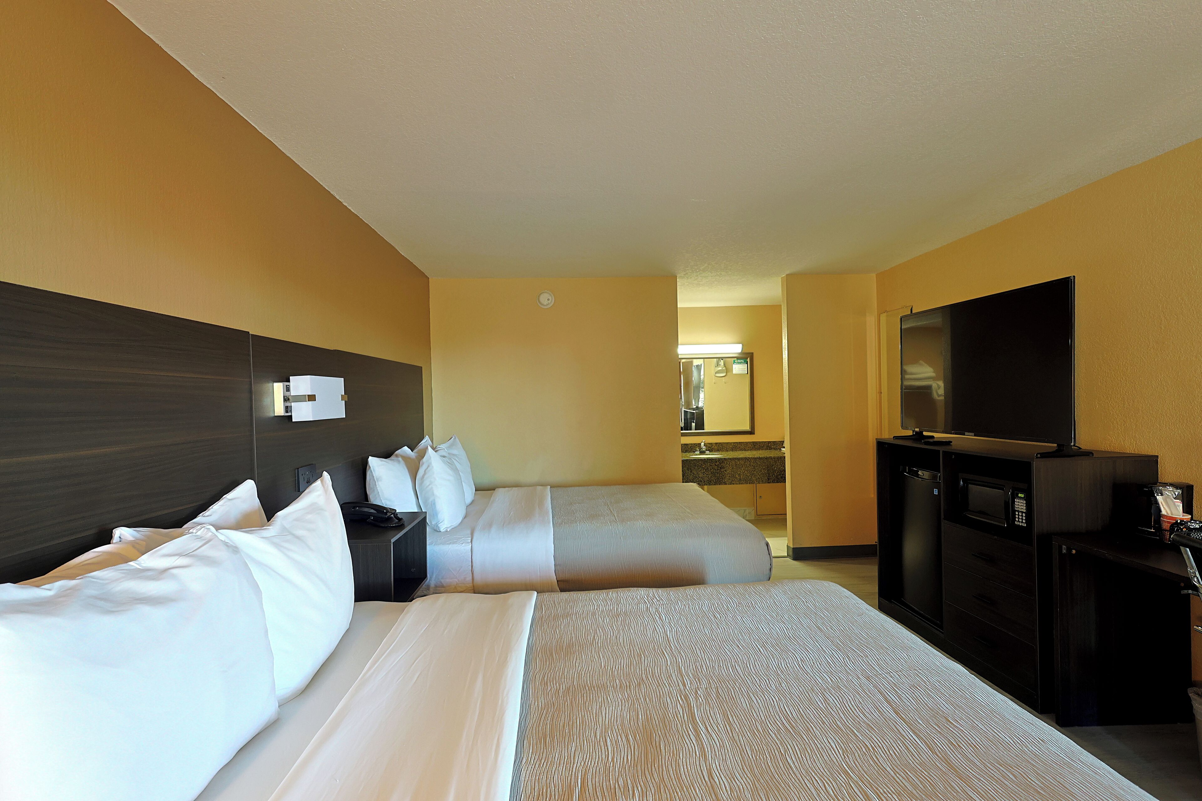 Habitación de hotel con dos camas, un escritorio con televisor y microondas.