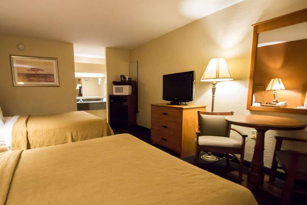 A hotel room with two beds, a desk, a chair, a television, a microwave, and a lamp.