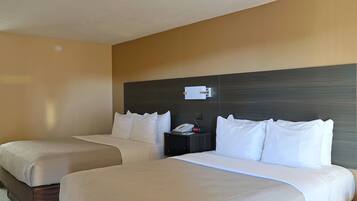 A hotel room with two beds, a nightstand with a phone, and a wall-mounted light fixture.