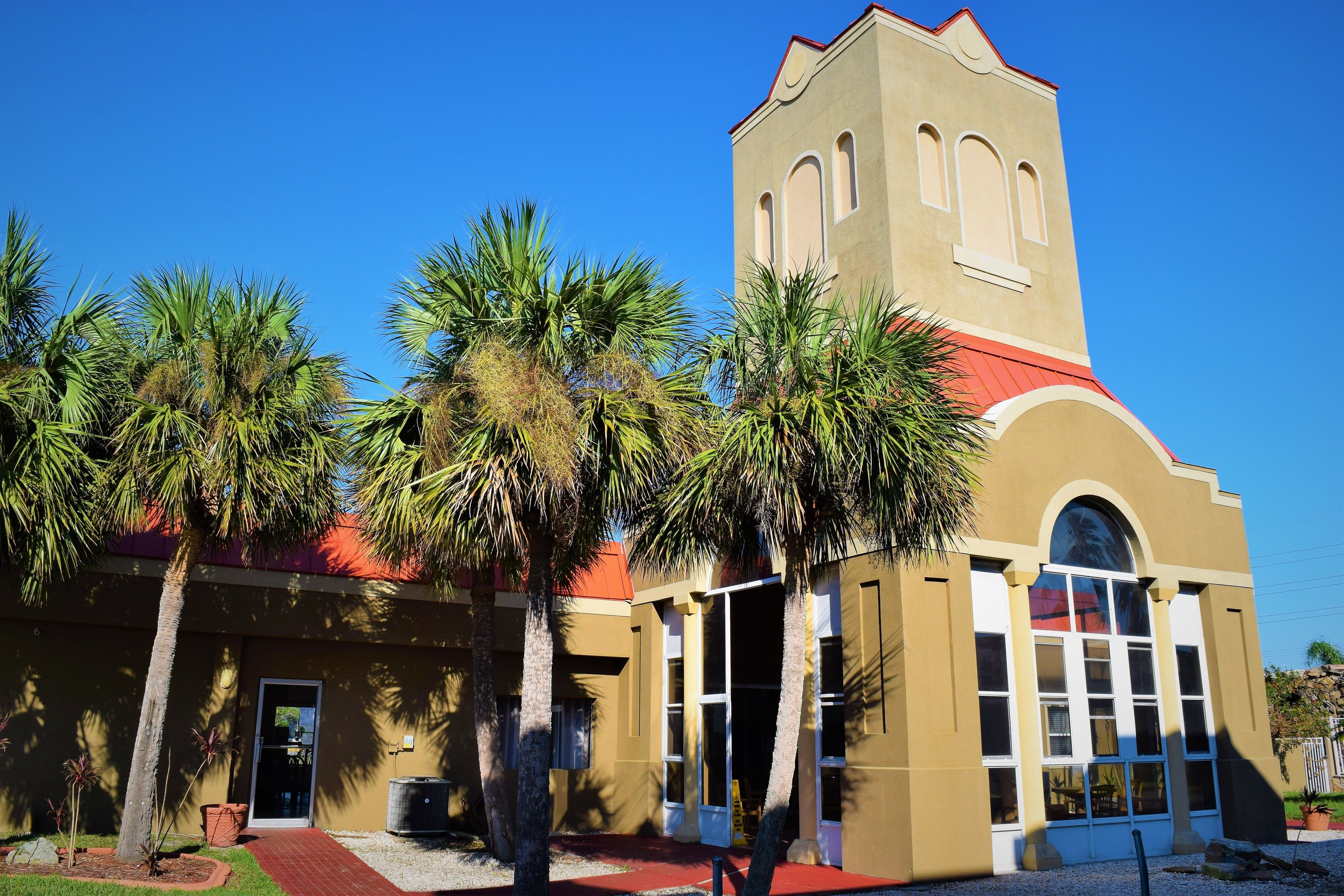 A building with a red roof, a bell tower, and palm trees in the foreground.