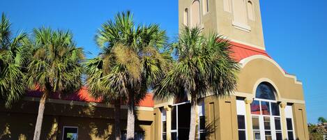 A building with a red roof, a bell tower, and palm trees in the foreground.