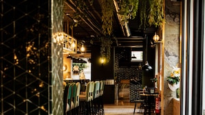 A restaurant with a long counter, chairs, hanging plants, and a tiled floor.