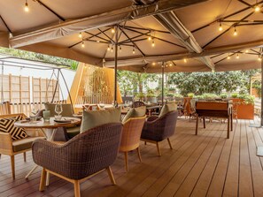 An outdoor dining area with wicker furniture, a piano, and string lights.