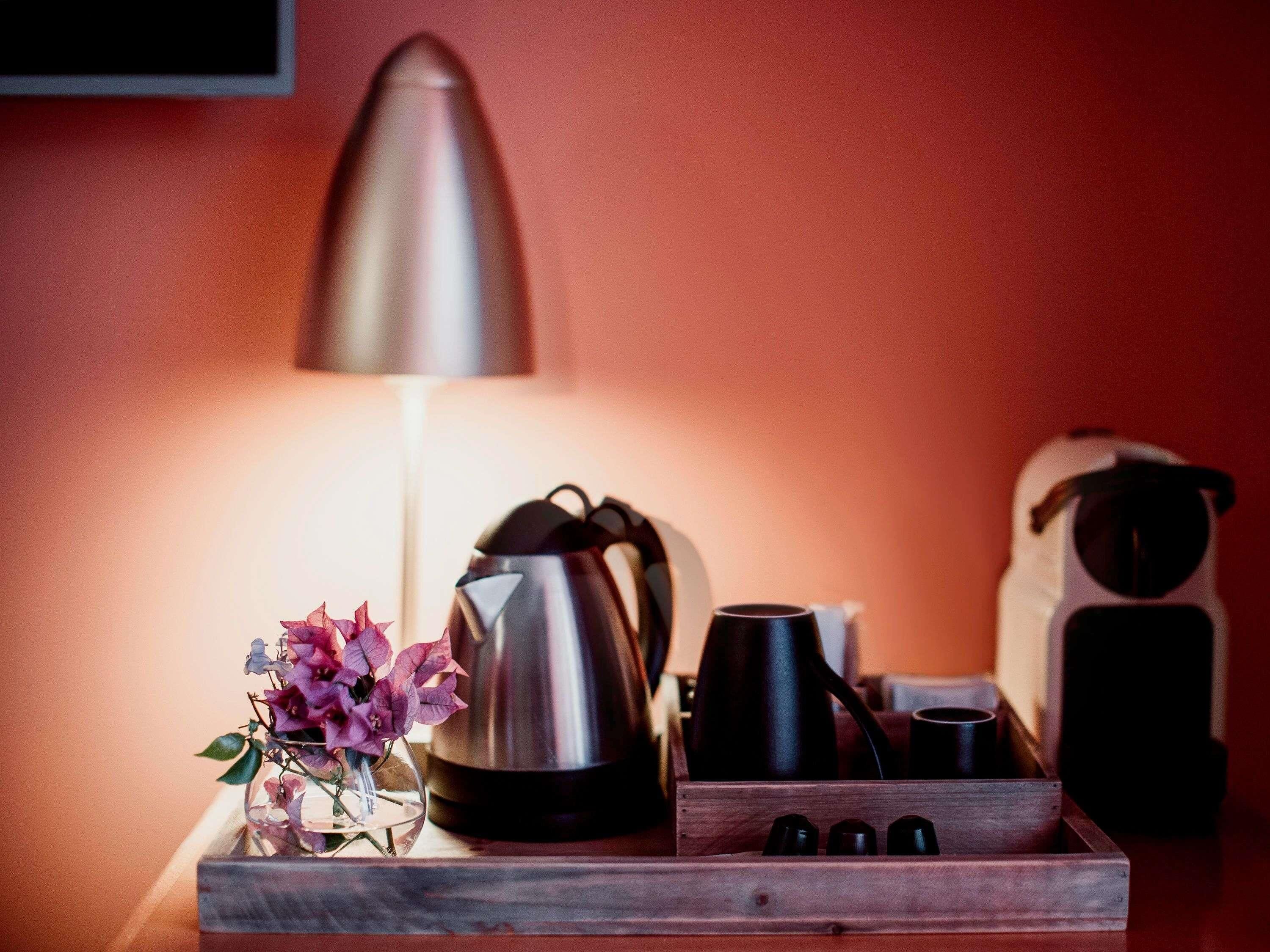 Eine Kaffeestation mit Wasserkocher, Tassen und einer Blumenanordnung auf einer Holztischplatte.