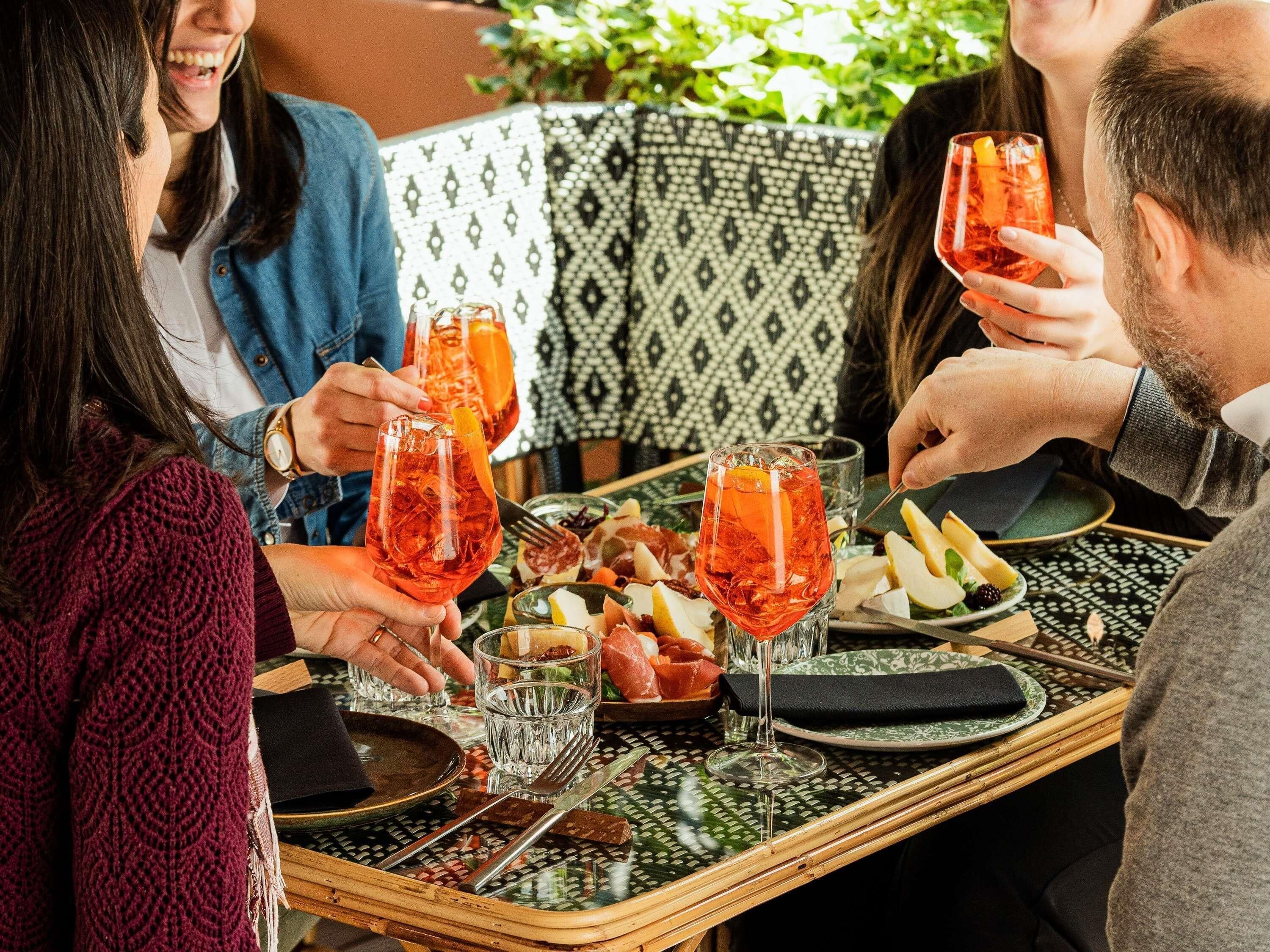 A group of people seated at a table with a patterned tablecloth, holding drinks and eating.