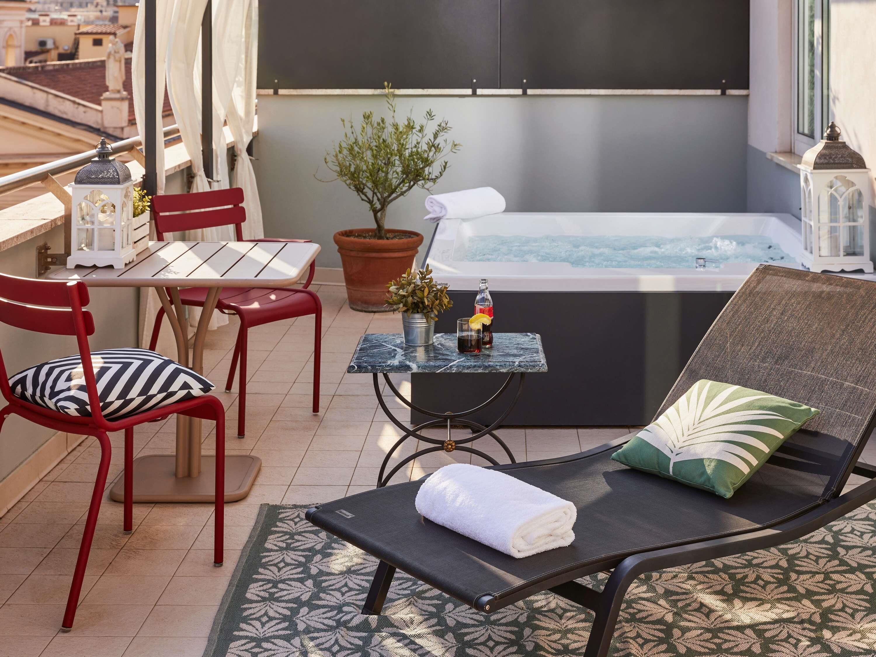 A balcony with a table, chairs, a lounge chair, a potted plant, and a hot tub.