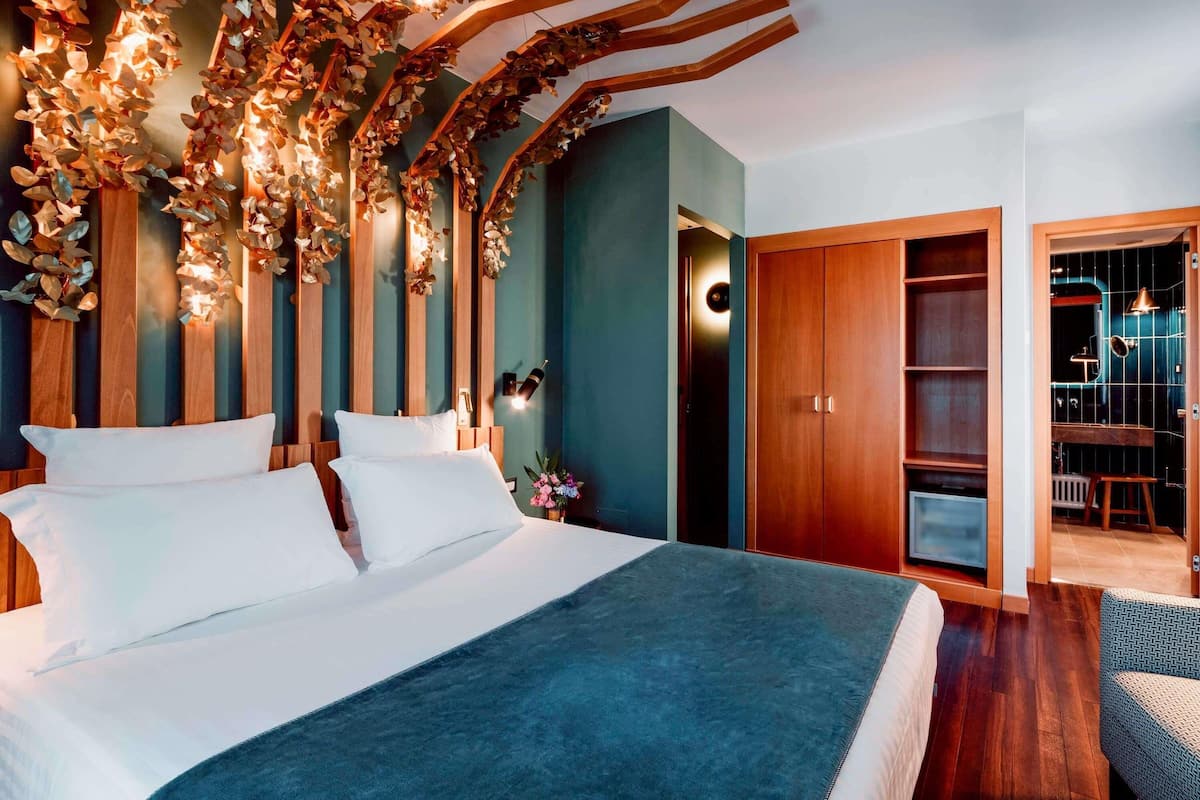 Une chambre à coucher avec un lit, des éléments de décoration murale en bois, une armoire et une salle de bain visible à travers une porte ouverte.