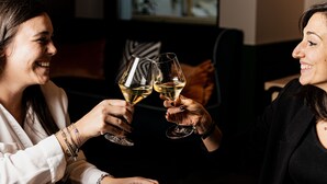 Two people toasting with wine glasses in a dimly lit room with a couch and a painting in the background.