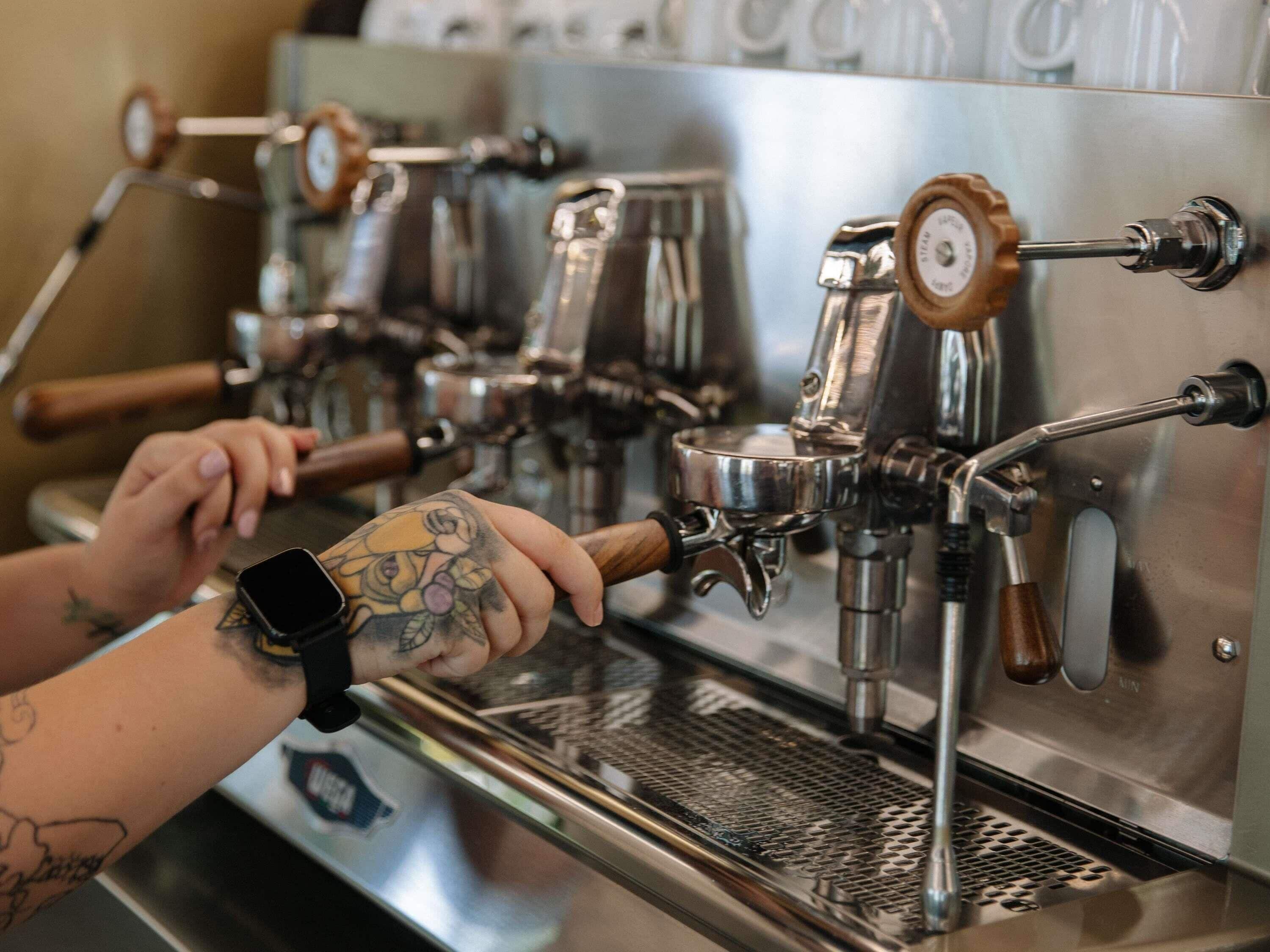 A coffee machine with multiple steam wands and a person operating it.
