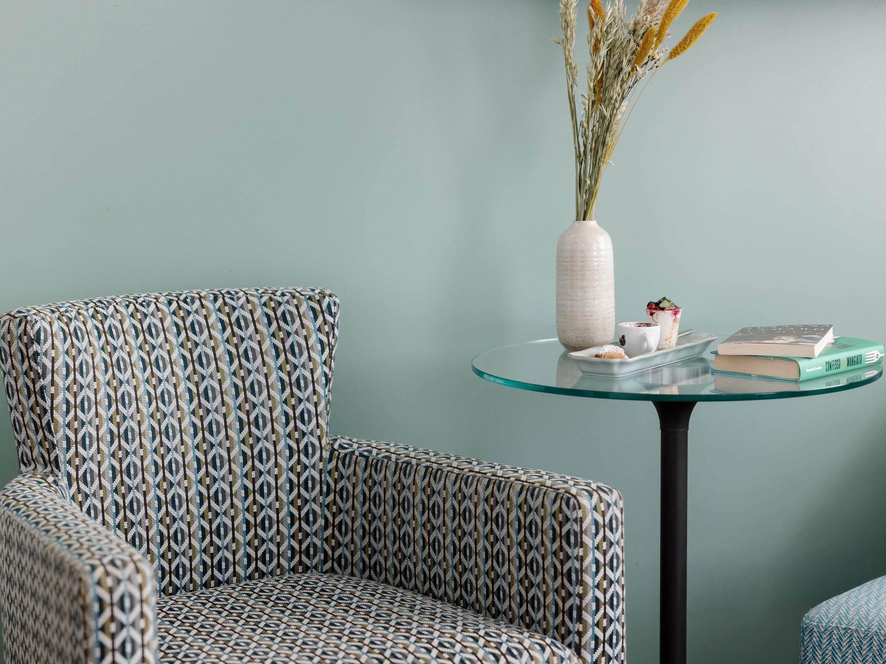 Een gestreept fauteuil, een glazen tafel met een vaas en boeken, en een effen muur.