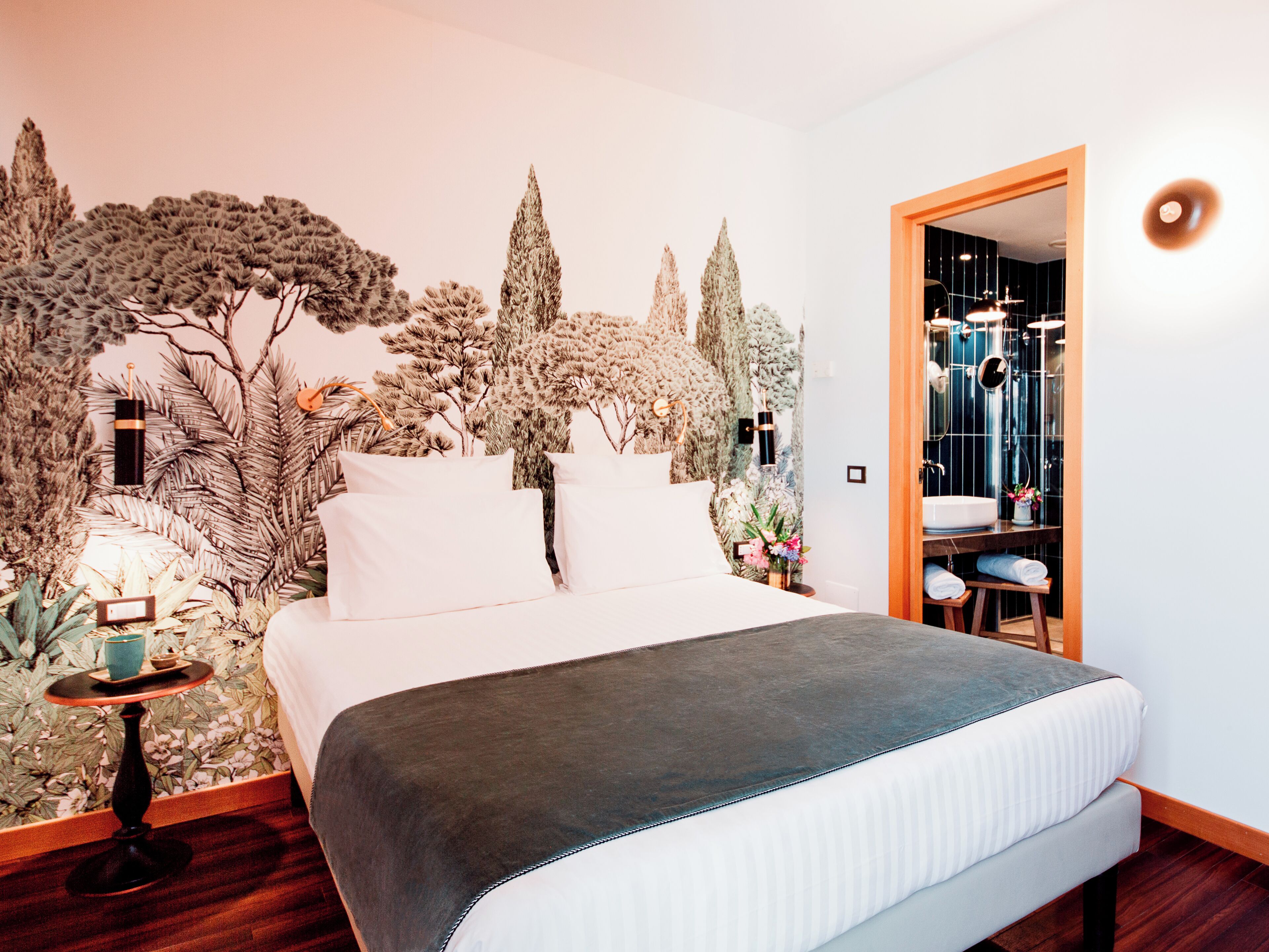 Quarto com cama, mesa de cabeceira, espelho e porta para um banheiro.