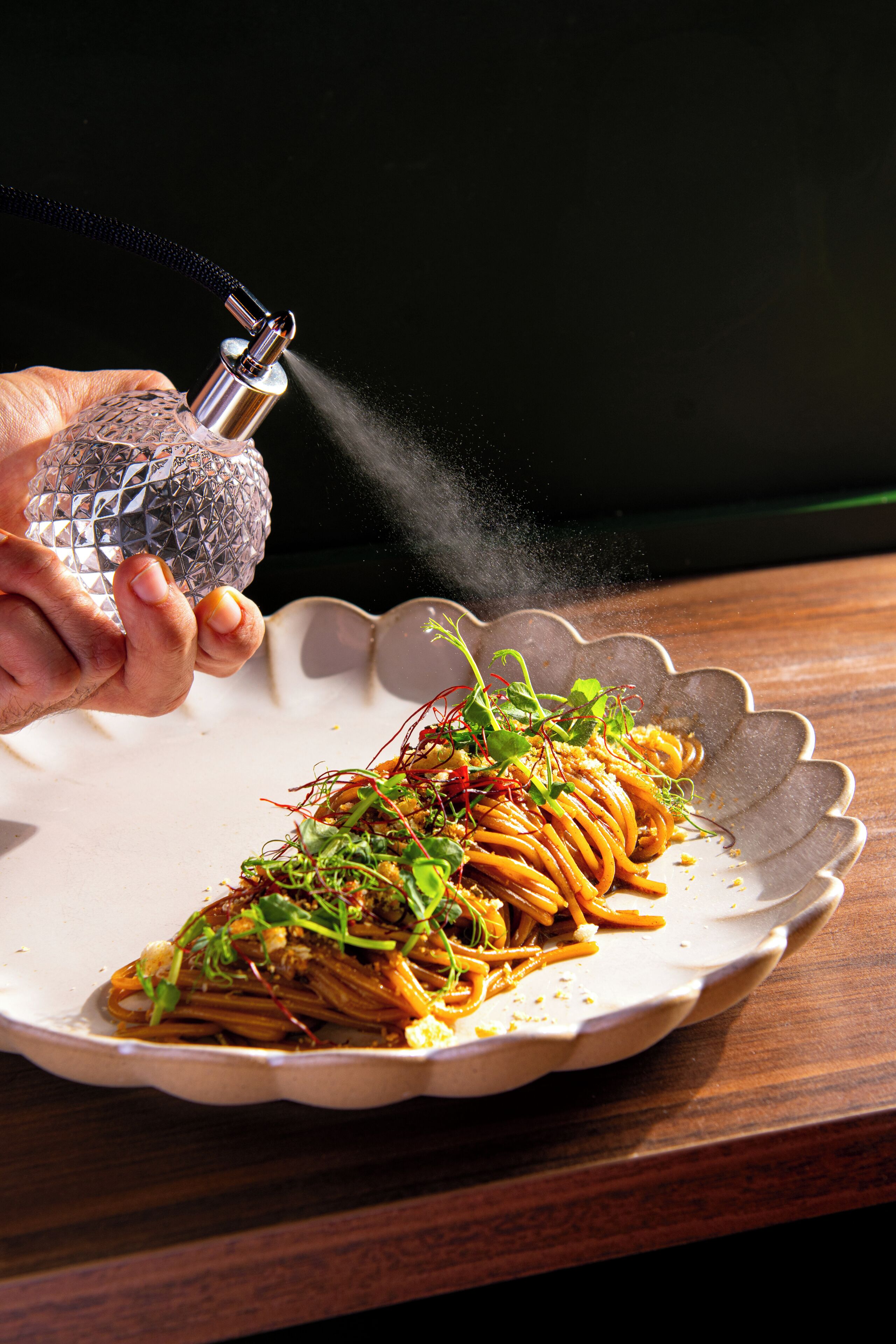 A hand sprinkling seasoning over a dish on a plate.