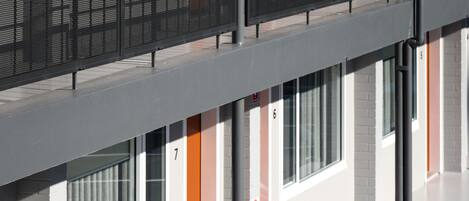 A modern building with numbered rooms, a red fire alarm box, and a clear view of the sky.