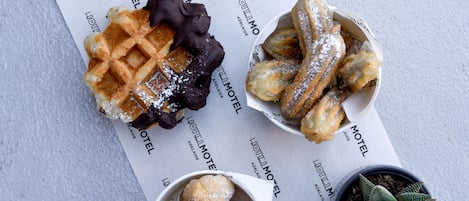 A waffle, churros, and pastries on a table with a menu and a small potted plant.