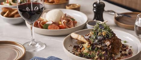 A dining table with plates of food, a glass of red wine, and cutlery.