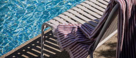 A poolside lounge chair with a striped towel draped over it.