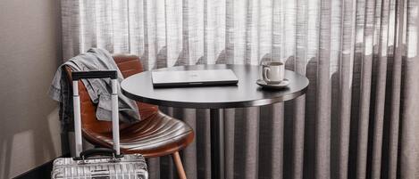 Habitación de hotel con una mesa redonda, una computadora portátil, una taza, una maleta y un sillón de cuero.