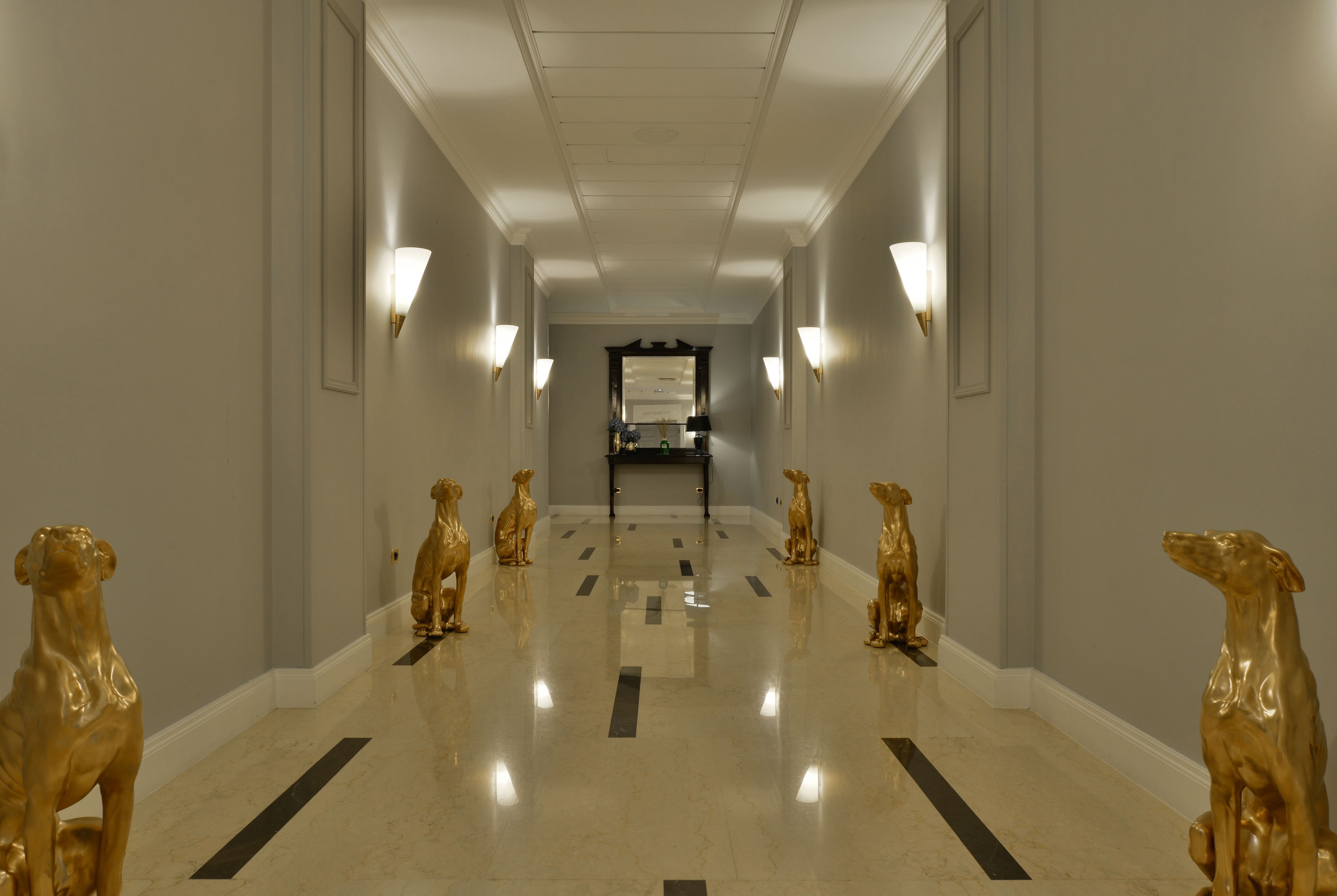 A hotel hallway with a polished floor, wall-mounted lights, and golden dog statues.