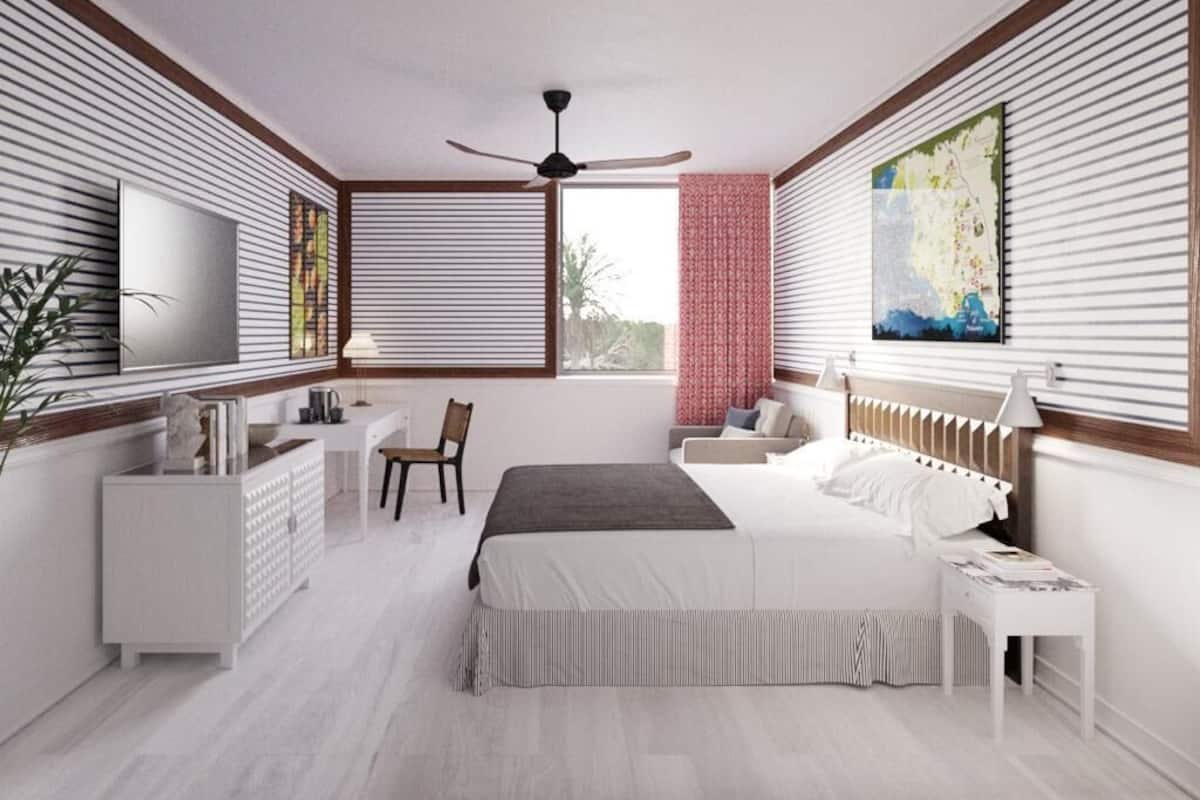 Een moderne slaapkamer met een groot bed, een bureau en een stoel. Er is een plafondventilator, een raam met zonwering en een schilderij aan de muur.