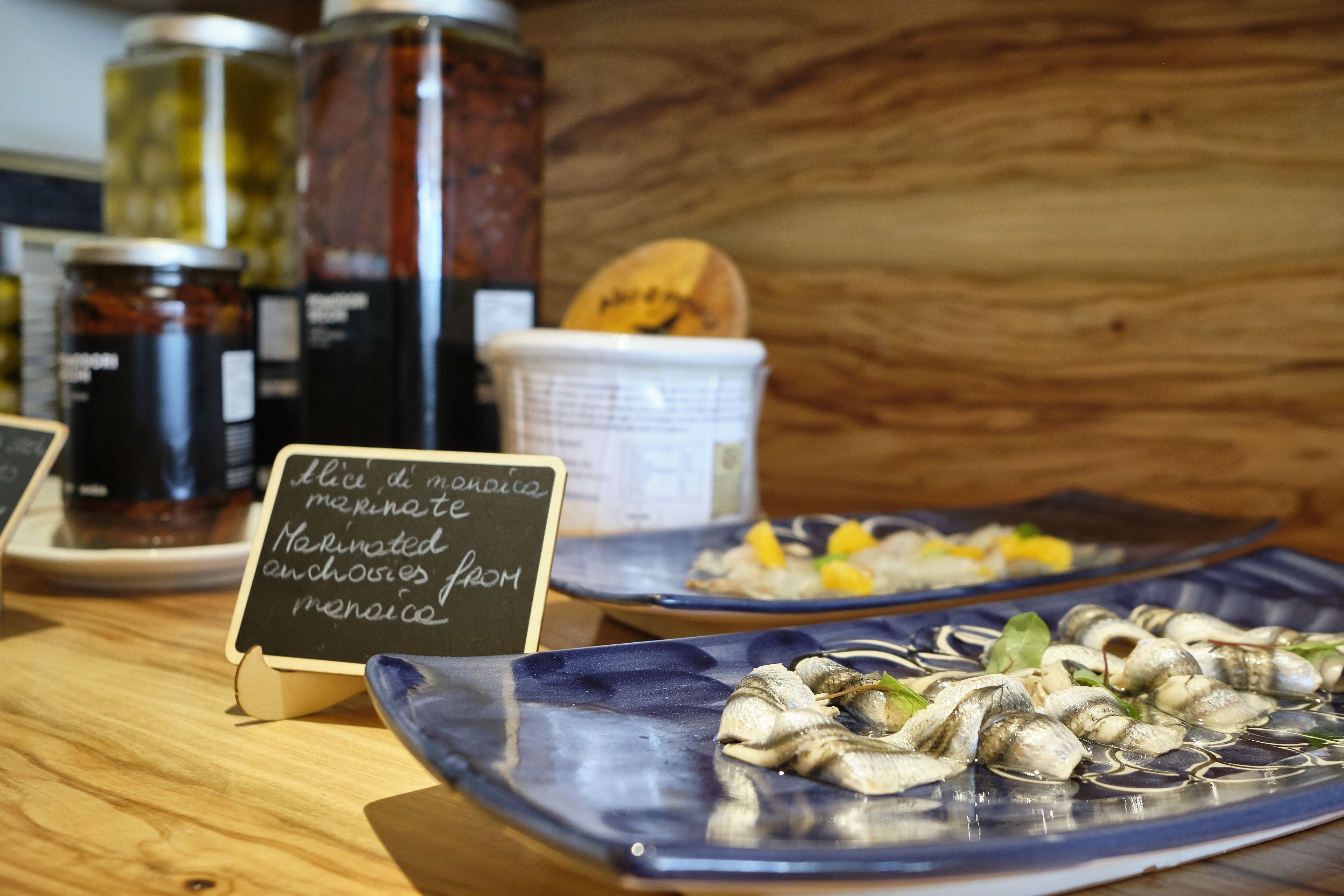 Una mesa de madera con frascos de pepinillos y un cartel que indica anchoas marinadas de meringa.