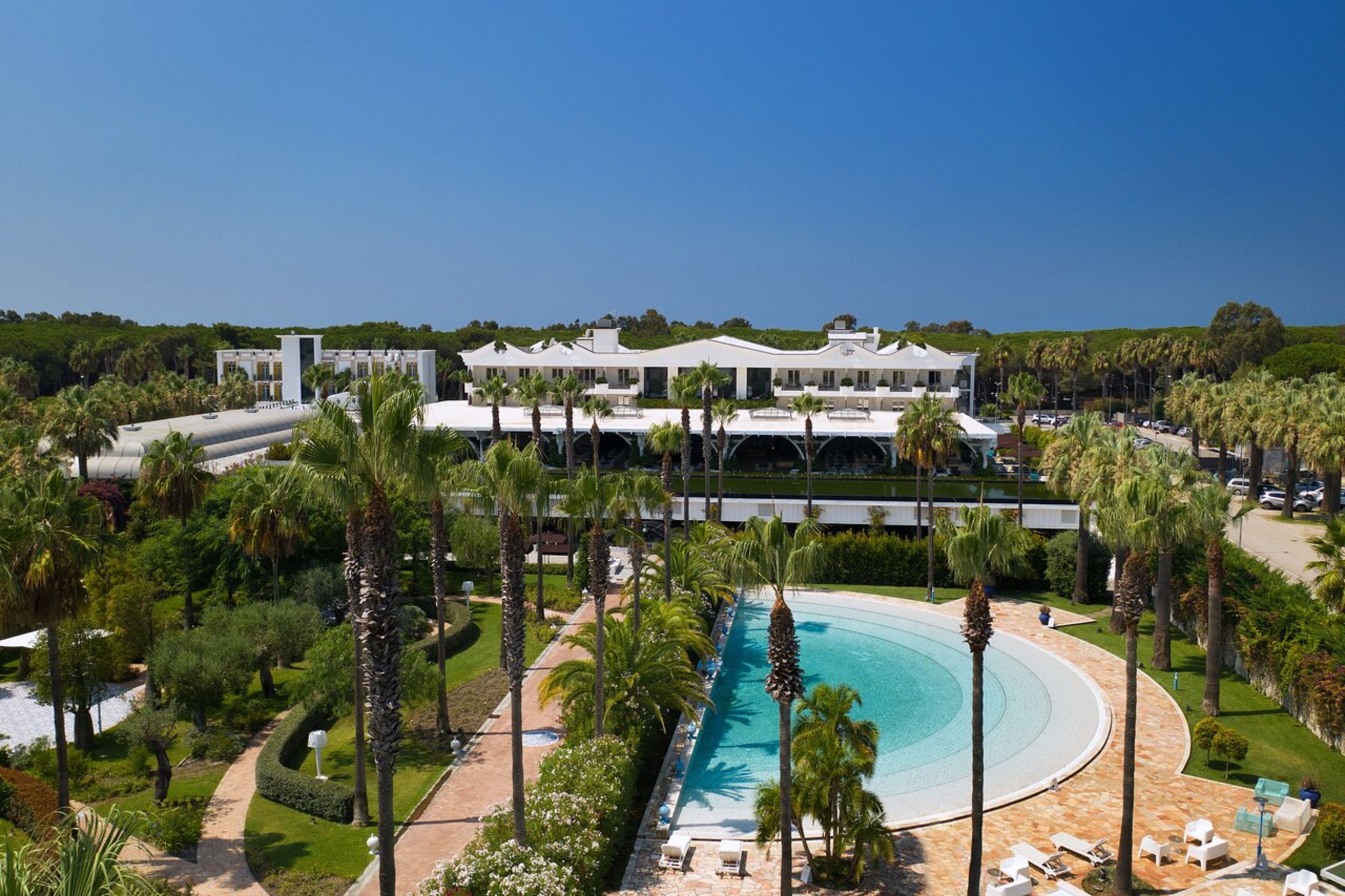A resort with a large swimming pool, palm trees, and a modern building with multiple balconies.