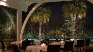 An outdoor dining area with tables set for two, surrounded by palm trees and a water feature. - Savoy Hotel & Spa (Capaccio-Paestum)