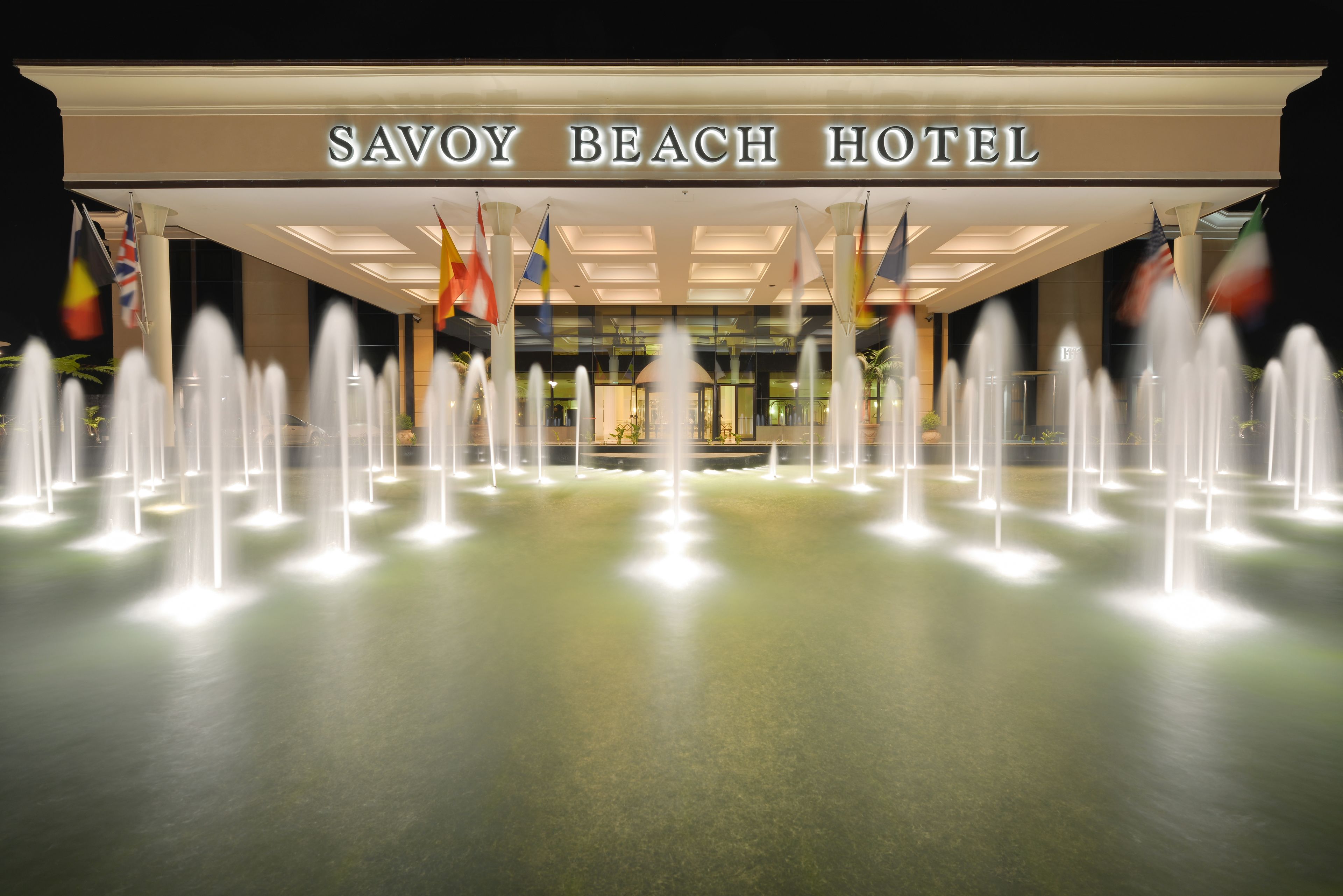 The exterior of the Savoy Beach Hotel with a fountain display in front.