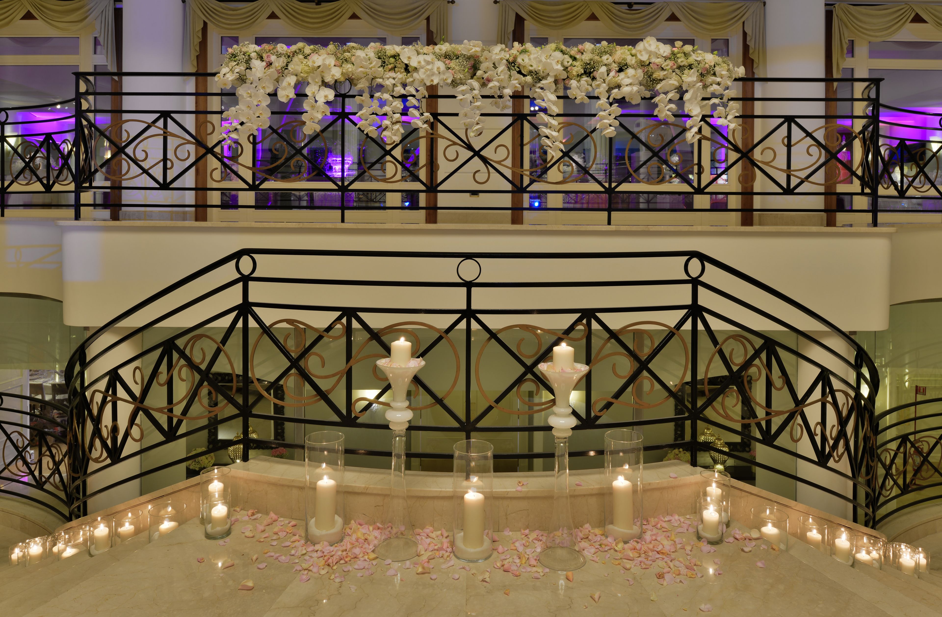A grand staircase with a railing, candles, and scattered rose petals.