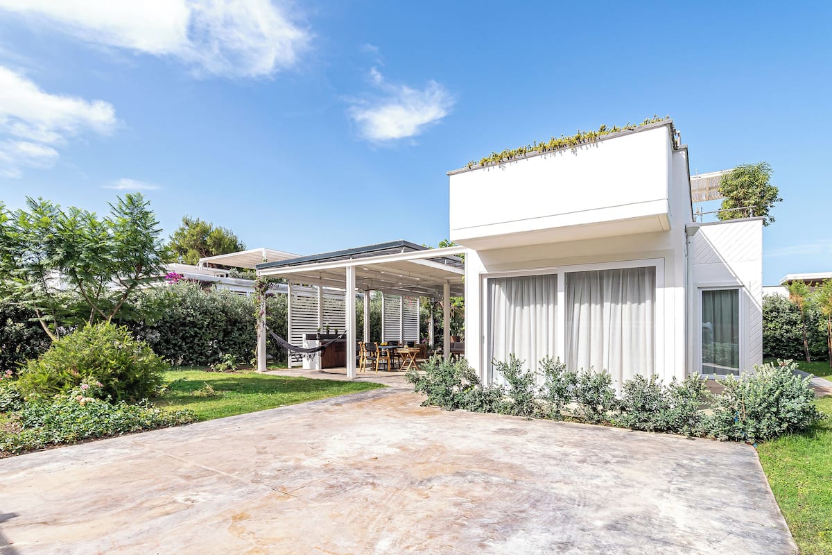 Een modern huis met een overdekt terras, een tuin en een helderblauwe lucht.