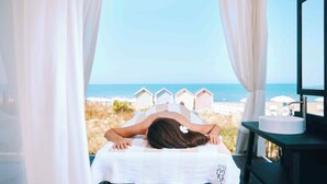 A person lying on a massage table with a view of the beach and beach huts. - Savoy Hotel & Spa (Capaccio-Paestum)