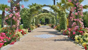A pathway lined with vibrant flowers and palm trees, leading to a covered area. - Savoy Hotel & Spa (Capaccio-Paestum)
