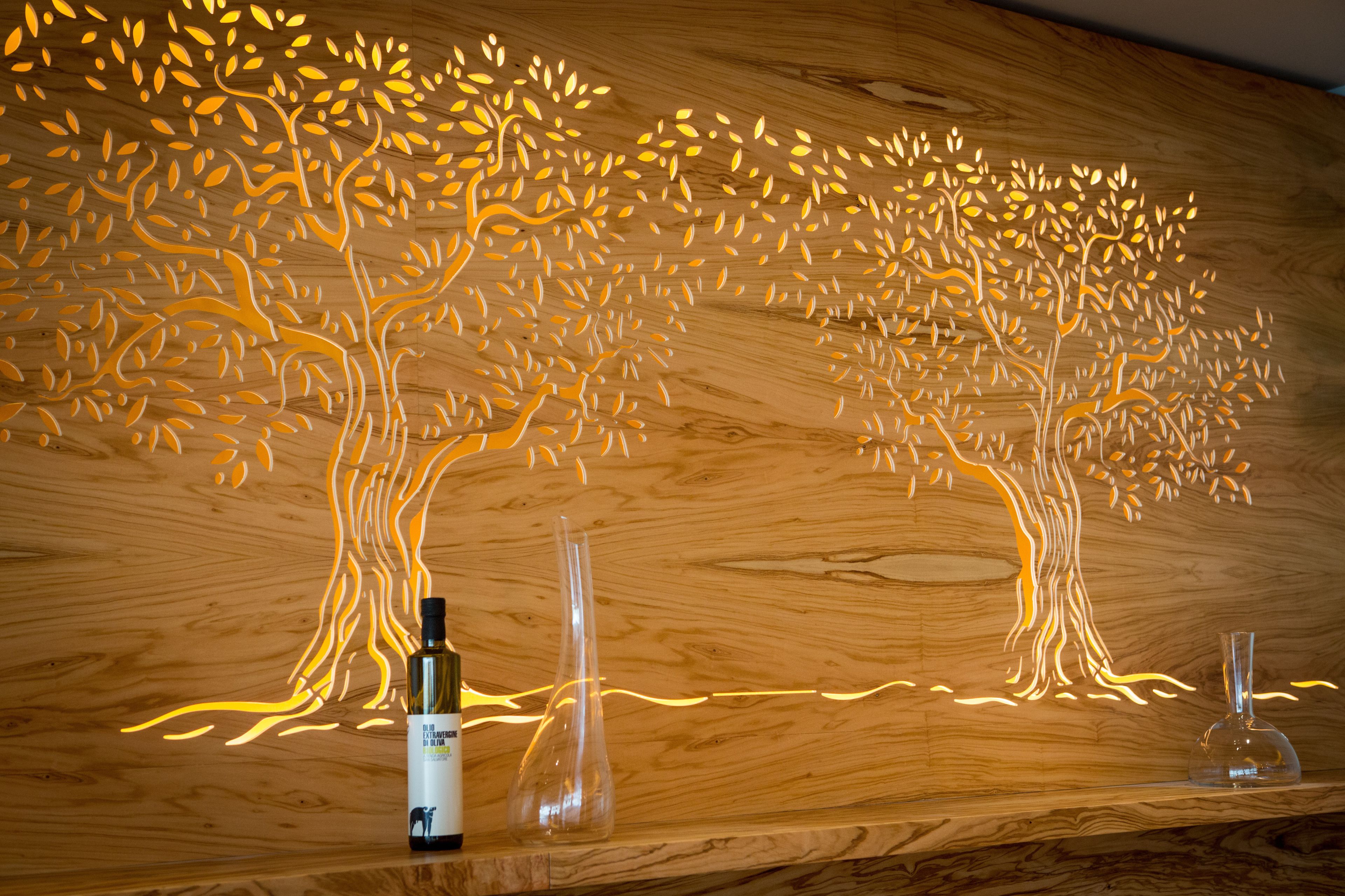 A wooden wall with a tree-like light installation and two clear glass vases on a shelf.