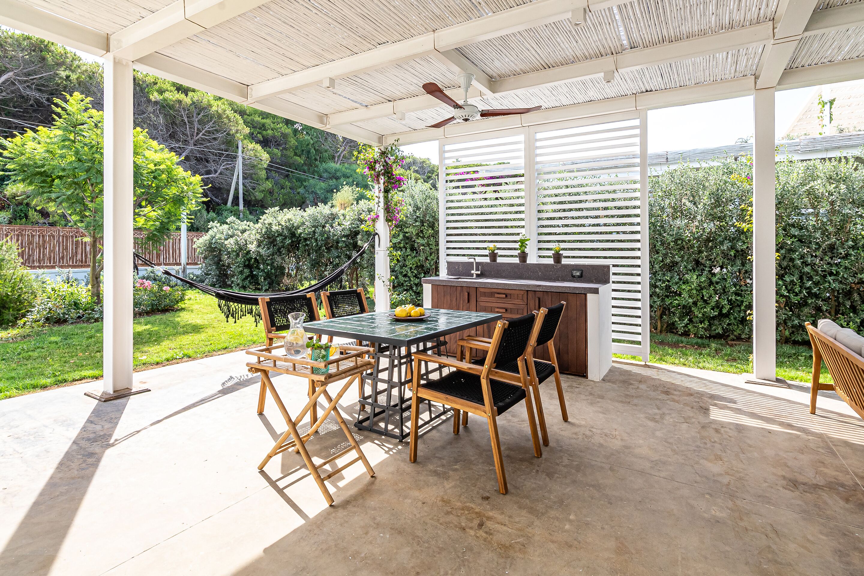 Une terrasse extérieure avec une table et des chaises, un hamac et un espace cuisine extérieur.